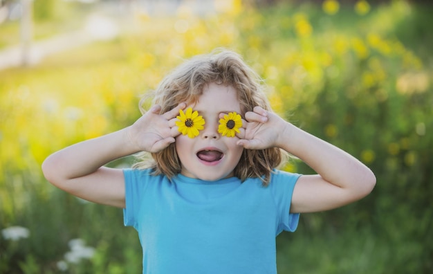 Portrait d'un drôle d'enfant garçon tenant des fleurs devant les yeux