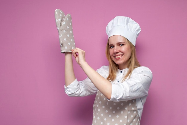 Portrait d'une drôle de fille cuisinier en tablier uniforme et gants pour la cuisson sur un fond coloré