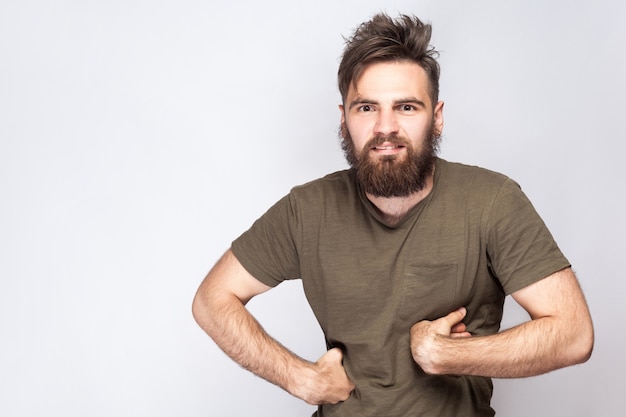 Portrait d'un drôle d'homme barbu fou avec un t-shirt vert foncé sur fond gris clair. tourné en studio. .