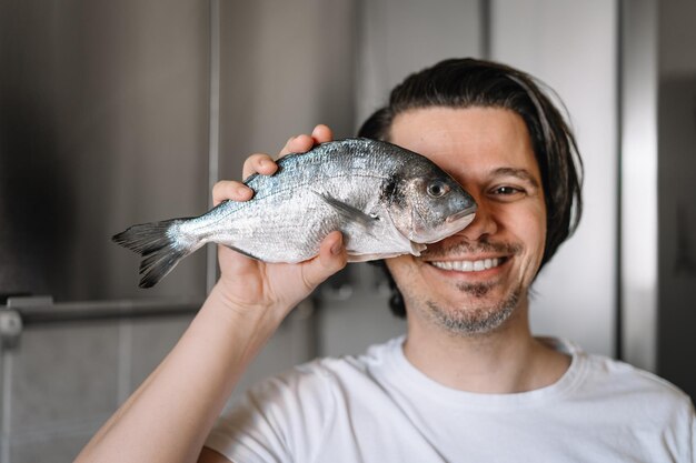 Photo portrait drôle d'un homme tenant un poisson dans la cuisine