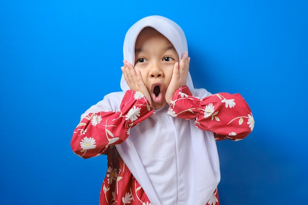 Portrait De Drôle De Jeune Fille Musulmane Asiatique Regardant La Caméra Avec De Grands Yeux Couvrant Sa Bouche, Expression Surprise Choquée Sur Fond Bleu