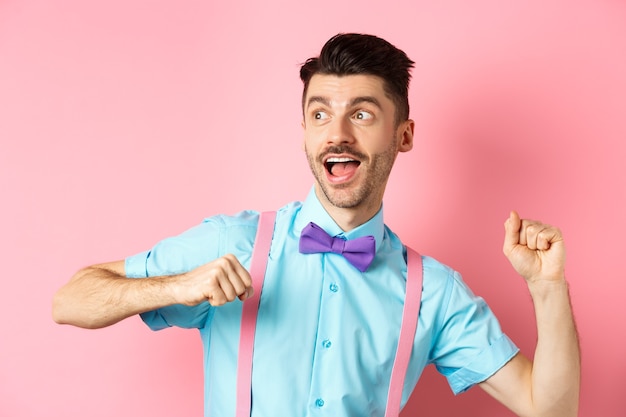 Portrait de drôle de jeune homme dépêchez-vous de courir, regardant de côté avec un visage excité, se précipitant pour obtenir une offre promotionnelle, debout sur le rose.