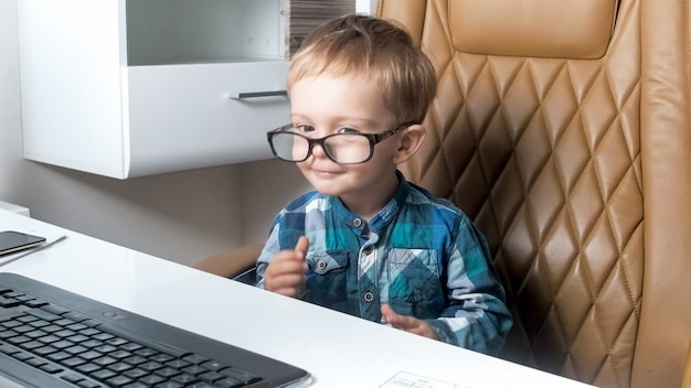 Portrait drôle de petit garçon portant des lunettes travaillant au bureau sur ordinateur.