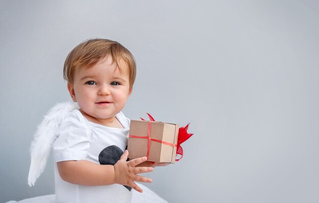 Portrait du bébé avec des ailes d'ange avec le cadeau en mains sur le gris