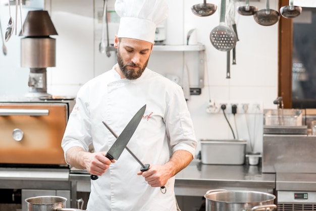 Portrait du chef cuisinier en uniforme avec des couteaux dans la cuisine du restaurant