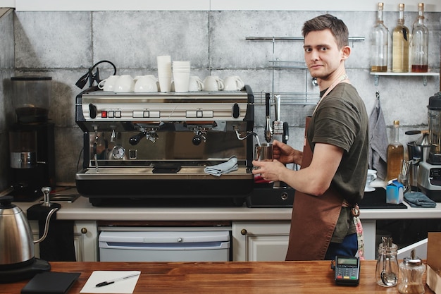 Le portrait du gars baristas au lieu de travail sur fond de café