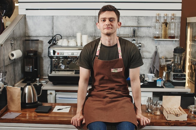 Le portrait du gars baristas au lieu de travail sur fond de café