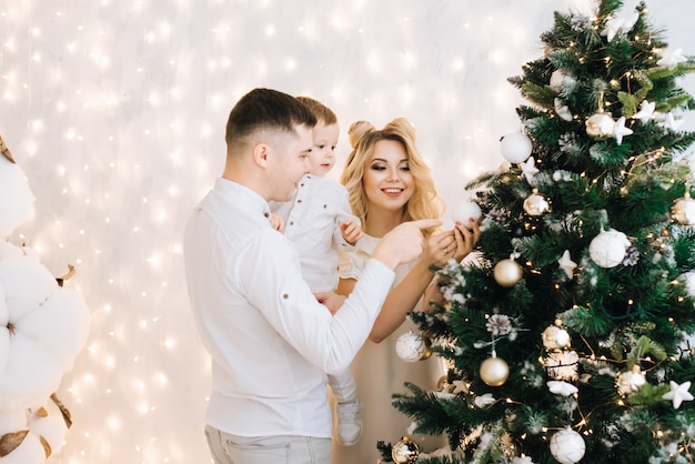 Portrait du nouvel an d'une belle jeune famille. Des parents attrayants et un petit fils décorent un arbre de Noël