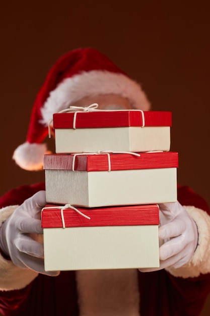 Portrait du père Noël tenant pile de coffrets cadeaux devant son visage