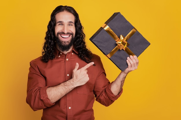 Portrait du promoteur guy tenir présent giftbox doigt direct sur fond jaune