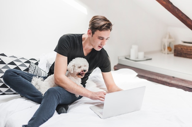 Photo portrait du propriétaire avec son chien mignon utilisant un ordinateur portable dans la chambre