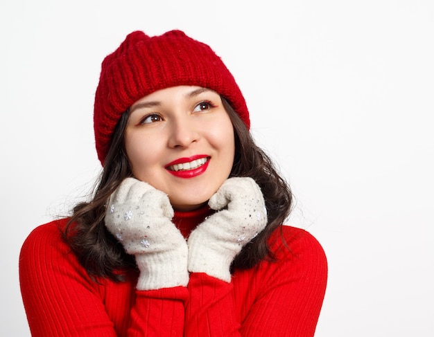 Photo portrait du visage de jolie jeune femme heureuse en bonnet tricoté rouge et pull sur blanc.