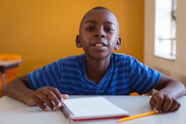 Portrait d'un écolier afro-américain assis au bureau avec un ordinateur portable en classe