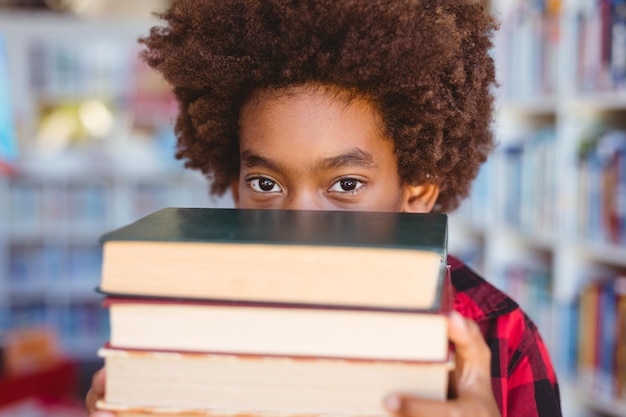 Photo portrait d'un écolier afro-américain transportant une pile de livres dans la bibliothèque de l'école