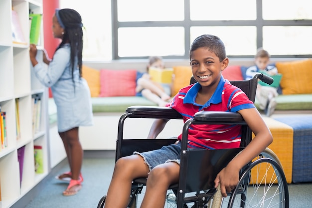 Portrait d'écolier handicapé en fauteuil roulant dans la bibliothèque