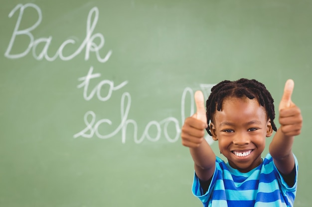 Portrait d'écolier souriant montrant les pouces vers le haut en classe