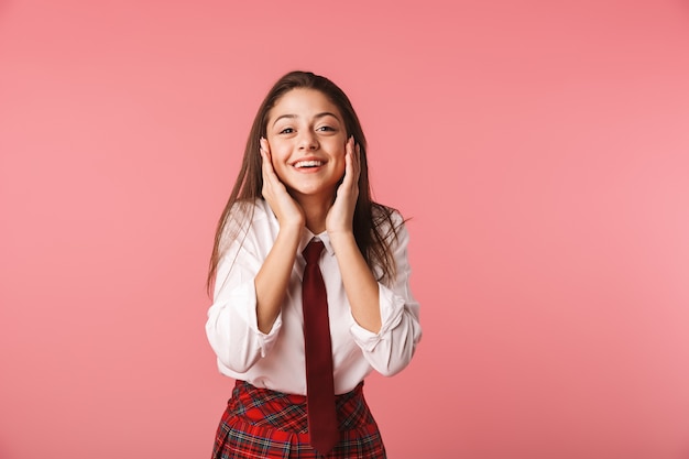 Portrait d'écolière de 15 à 16 ans en uniforme scolaire debout, isolé sur mur rouge