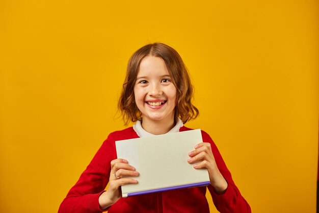 Portrait d'écolière adolescente heureuse couvrir son visage par livre