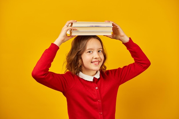 Portrait d'écolière adolescente heureuse en uniforme tenant des livres sur la tête