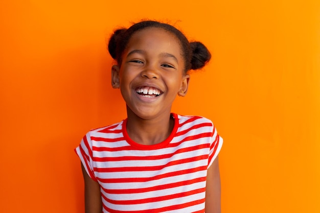 Portrait d'une écolière afro-américaine heureuse qui rit sur un fond orange à l'école primaire