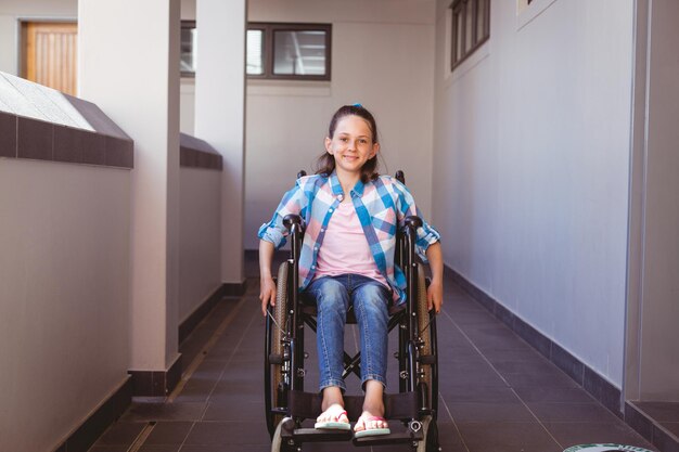 Portrait d'une écolière caucasienne handicapée souriante assise en fauteuil roulant dans le couloir de l'école