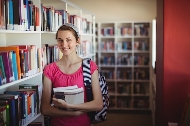 Portrait d'écolière debout avec des livres dans la bibliothèque