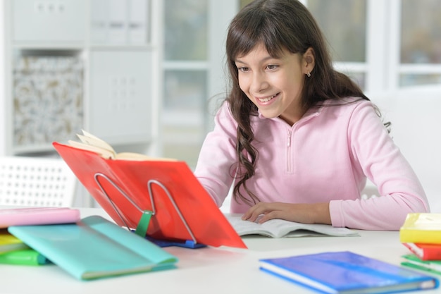 Portrait d'une écolière heureuse assise au bureau et étudiant