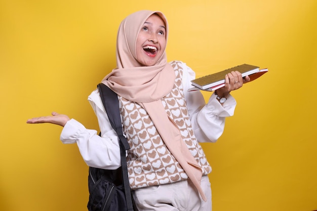 Portrait d'une écolière musulmane asiatique souriante avec hijab et sac à dos noir tenant un livre montrant ha