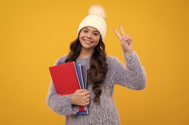 Portrait d'une écolière rêveuse dans un chapeau d'automne avec des livres isolés sur un fond jaune Vacances d'hiver pour enfants Face à une fille heureuse émotions positives et souriantes