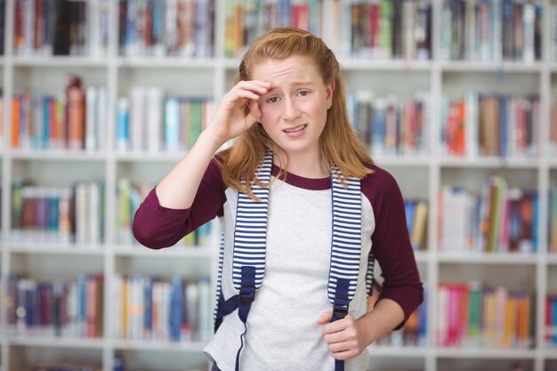 Portrait d'écolière triste debout avec cartable dans la bibliothèque