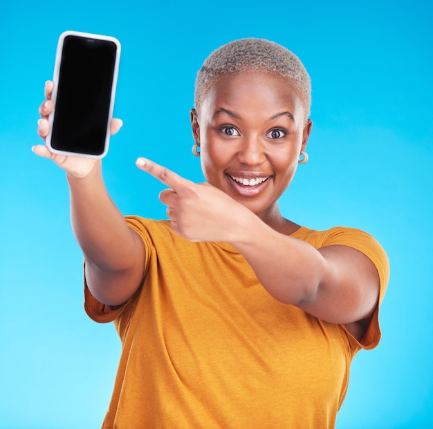 Photo portrait d'un écran de téléphone et d'une femme noire heureuse pointant vers l'espace publicitaire du studio, la promotion de l'application en ligne ou les actualités web.