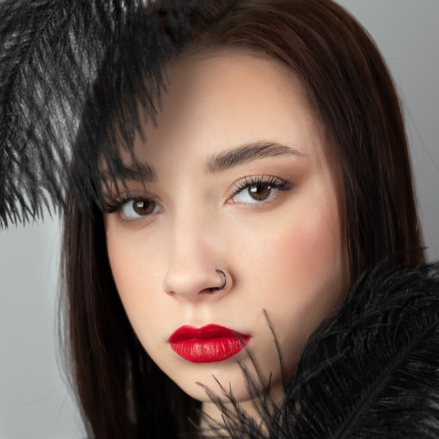Portrait élégant et créatif d'une fille modèle caucasienne avec des lèvres rouges et des plumes noires autour de la tête, vue latérale. Notion de beauté.