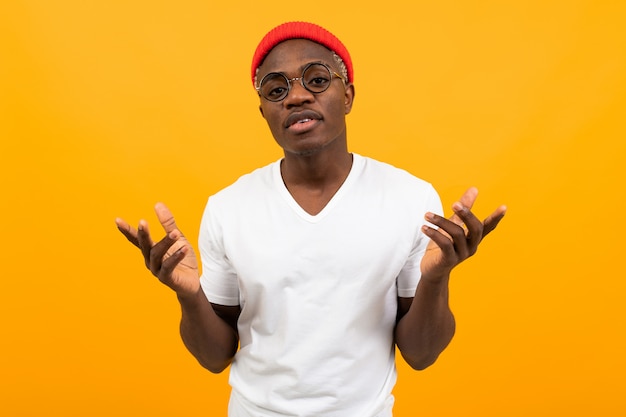 Portrait d'un élégant homme noir africain sexy dans un t-shirt blanc avec des lunettes hausser les mains sur jaune