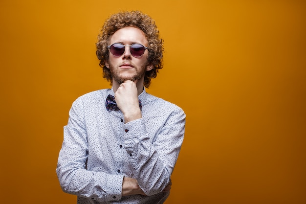 Portrait d'élégant jeune homme à lunettes de soleil sur fond jaune