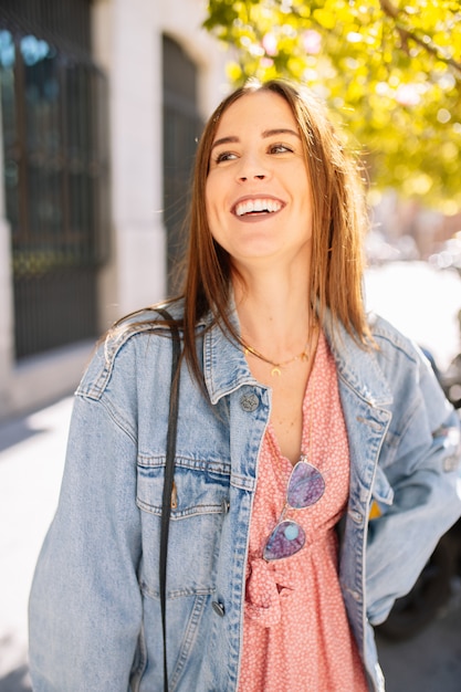 Portrait d'élégante souriante heureuse jeune femme dans la rue avec des dents blanches parfaites. Tendance de la mode été et printemps, veste en jean, lunettes de soleil, gaie, positive, qui rit. Modes de vie.