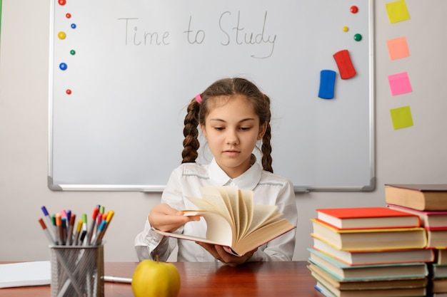 portrait d'une élève de l'école joyeuse regardant à travers le livre en choisissant le texte à lire