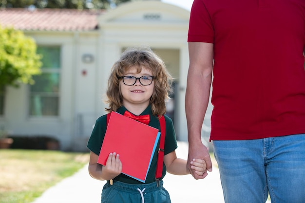 Portrait d'un élève nerd heureux tenant la main des enseignants père et fils marchant dans le parc de l'école tenant