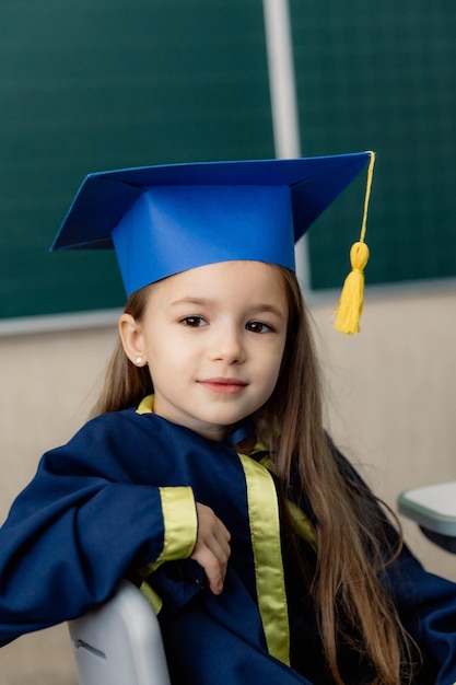 portrait d'un élève de première année dans un chapeau de fête posant pour une photo à un bureau dans une salle de classe