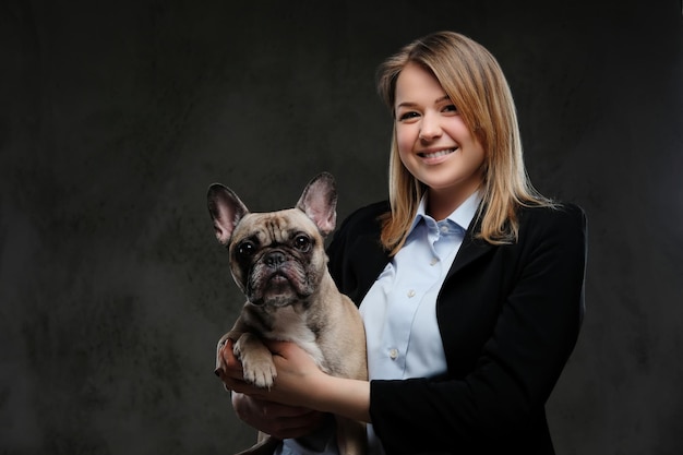 Portrait d'un éleveur de femme blonde souriante tient son mignon carlin. Isolé sur un fond texturé sombre.