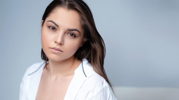 Portrait émotionnel en gros plan d'une fille triste regardant la caméra sur un fond gris Belle femme naturelle avec une peau naturelle