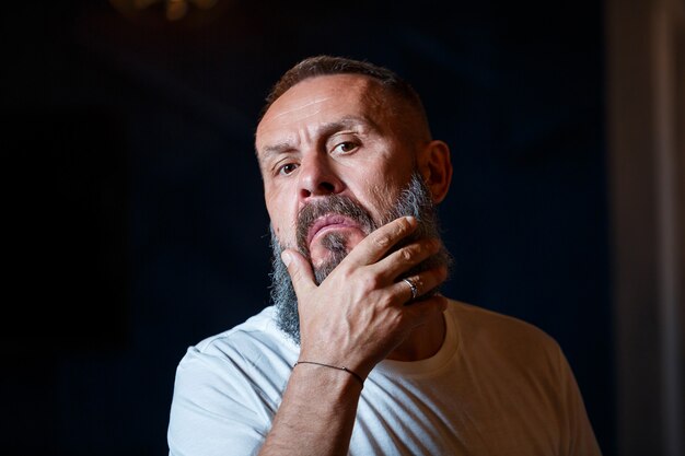 Portrait émotionnel d'un homme aux cheveux gris adulte avec une barbe dans un t-shirt blanc