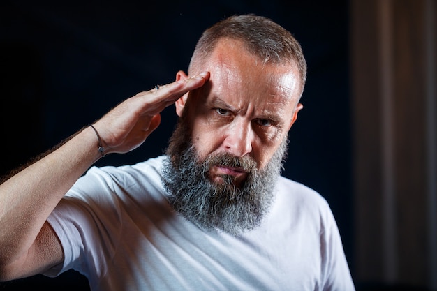 Portrait émotionnel d'un homme aux cheveux gris adulte avec une barbe dans un t-shirt blanc