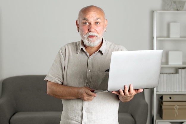 Portrait d'un employé de bureau senior avec un ordinateur portable Un homme âgé avec une barbe grise a un travail dans un ordinateur portable à la maison ou au bureau Homme mûr utilisant un ordinateur Directeur général âgé