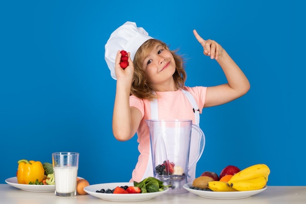 Portrait d'un enfant âgé d'un an en casquette et tablier de cuisinier faisant de la salade de fruits et cuisinant des smoothies aux framboises