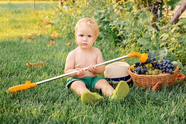 Portrait enfant blond garçon jouant avec pulvérisateur et raisins dans le jardin