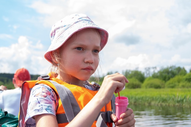 Portrait d'un enfant dans un gilet de sauvetage orange soufflant des bulles de savon flottant sur un bateau avec ses parents