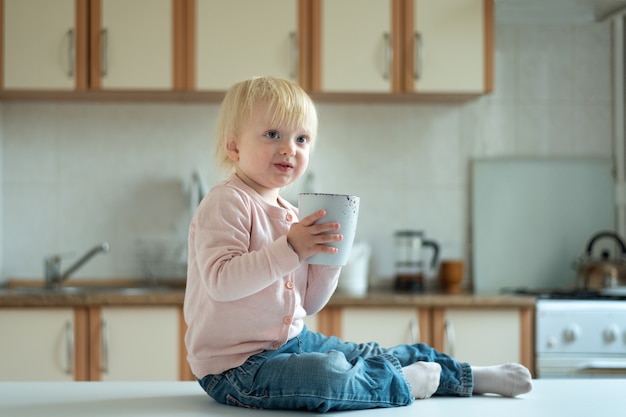 Portrait d'un enfant de deux ans blond mignon dans la cuisine avec une grande tasse.