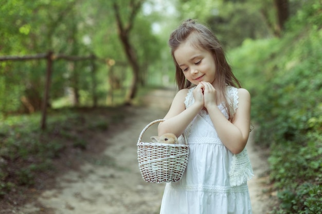 Portrait d'une enfant fille dans une forêt féerique Elle tient un panier avec un petit lapin