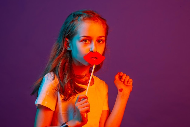 Portrait d'une enfant fille La fille a mis des lèvres de papier sur ses lèvres sur un fond violet