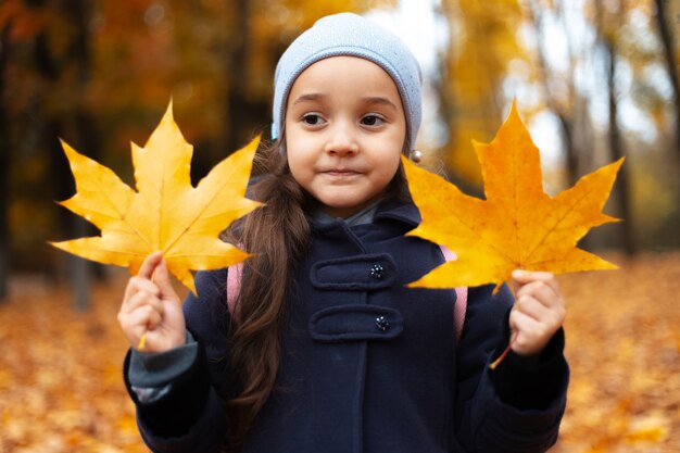 Portrait d'enfant gai tenant deux feuilles d'automne jaunes sèches dans les mains.
